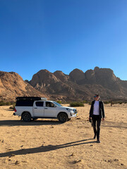 Young man with binoculars and car in desert. SUV off road auto vehicle.