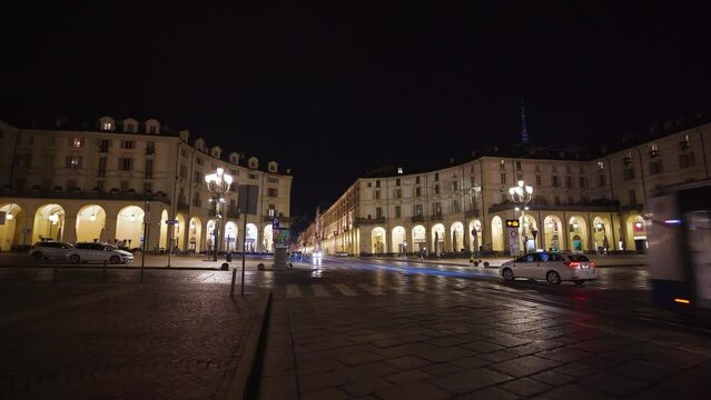 Moving shot of a bus and a taxi passing by in a square without people. Turin city at night in Italy. Illuminated streets in the evening, empty square with historical monuments