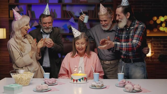 Birthday Elderly Party, 60th Anniversary. Group of Mature People Celebrating Senior Woman Birthday at Home with Cake and Candle Lights. Old Friends Clapping Hands at Dinner Table