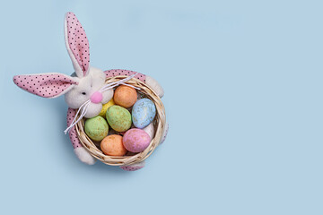 Easter basket with plush bunny and decorated eggs on pastel blue background