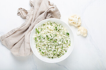 Raw cauliflower rice or couscous with dill in white bowl, healthy low carbohydrates vegetable side...