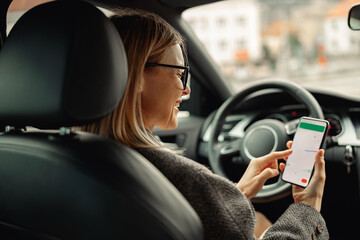 Female driver in glasses using phone with gps navigation app on screen while traveling by car