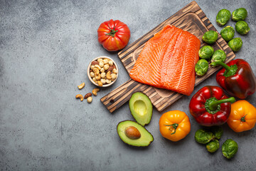 Fresh raw salmon fillet on wooden cutting board, organic bio vegetables and nuts on rustic stone grey background top view. Ingredients full of vitamins for healthy diet and nutrition, space for text