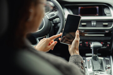 Close up of businesswoman hands is using phone while sitting behind steering wheel in own car