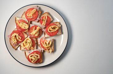 Sourdough Canape with butter, ham, tomato and egg served on a white plate. 