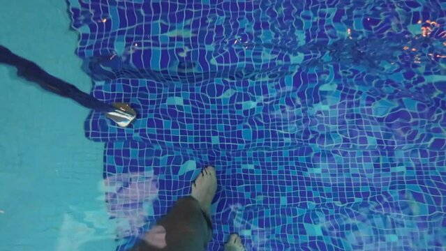 Man enter or exit swimming pool by steps. POV male barefoot legs.