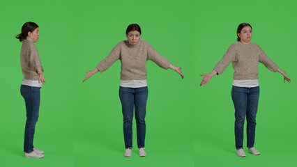 Naklejka premium Doubtful girl doing i dont know sign in studio, acting clueless and uncertain about question over full body greenscreen. Young adult being unsure and confused, shrugging over green screen.