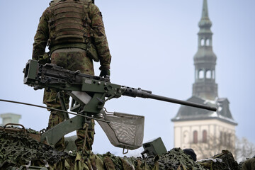 Fototapeta na wymiar Estonian military soldier on an armored personnel carrier with a heavy machine gun on the roof, view from the back with Tallinn in the background.