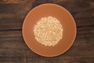 A ceramic bowl with raw oats on a wooden background