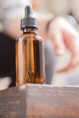 A dropper bottle on a wooden table with a person out of focus behind it