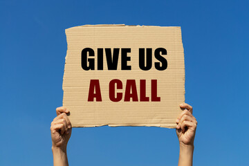 Give us a call text on box paper held by 2 hands with isolated blue sky background. This message board can be used as business concept to inform audience to call to us.