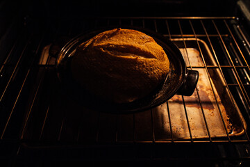 sourdough loaf baking in oven on black ceramic part of bread cloche	