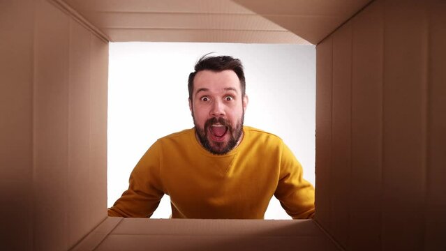Young excited man emotionally opening cardboard box and looking inside with happiness and excitement. Good present. Concept of shopping, delivery, emotions and facial expression, food, gift