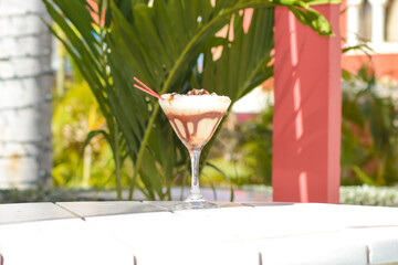 A cream caramel cocktail drink on the table with palm leaves in the background. 