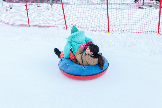 two girls sledding on snow slope in one snow bob
