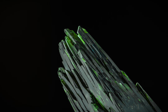 dark green aegirine crystal on black background. macro detail texture background. close-up raw rough unpolished semi-precious gemstone