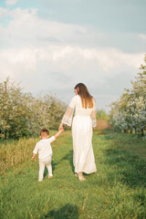 Portrait of happy mother and her baby boy. Beautiful touching scene of mom and son. Blooming garden in spring.