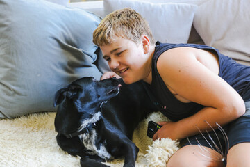 Teen boy snuggling on couch with pet dog. Man's best friend. Black kelpie x labrador breed.