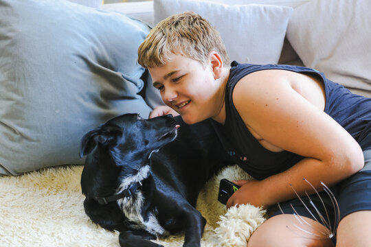 Teen boy snuggling on couch with pet dog. Man's best friend. Black kelpie x labrador breed.