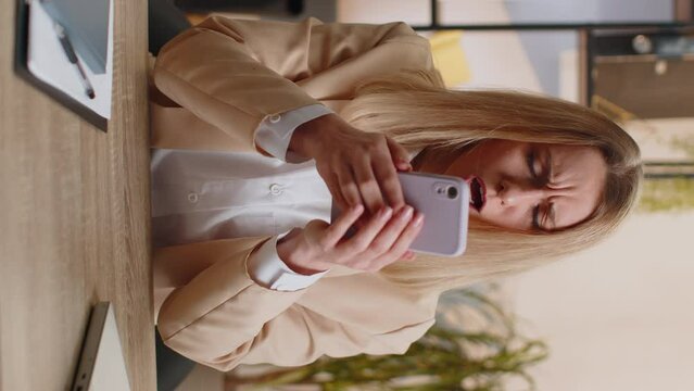 Businesswoman in suit use smartphone typing browsing, loses becoming surprised sudden lottery results, bad news, fortune loss fail at home office desk workplace. Freelancer worker woman. Vertical shot