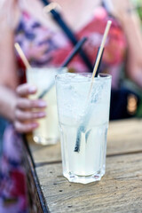 two cocktails with straws on a table and a woman in blurred background