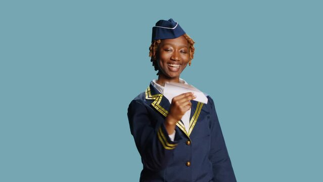 Young stewardess playing with paper airplane, having fun showing origami small plane on camera. Air hostess in flying uniform holding folded aviation aircraft, female model with confidence.