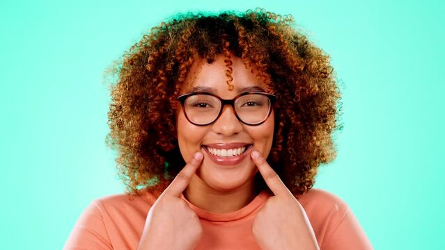 Face, black woman and pointing to mouth, smile and happiness against a blue studio background. Portrait, Jamaican female and lady show to teeth, whitening and happiness with confidence and wellness
