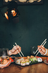 A white man and a black woman eat delicious fresh sushi and drink wine. Lunch at a Japanese restaurant. Asian cuisine.