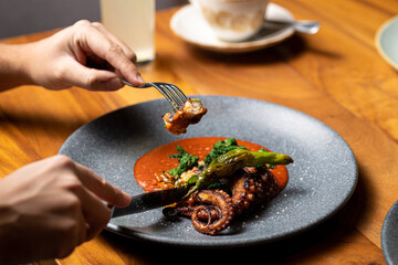 Delicious grilled octopus dish, piece grabbed with a fork, in luxurious restaurant, horizontal view.