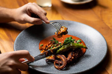 Delicious grilled octopus dish, piece grabbed with a fork, in luxurious restaurant