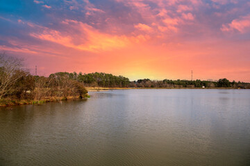 A gorgeous winter landscape with a rippling lake surrounded by red trees, lush green trees and...