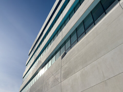 The exterior wall of a contemporary commercial style building with concrete prefabricated panels and glass windows. The futuristic building has engineered cement cladding frame panels. 