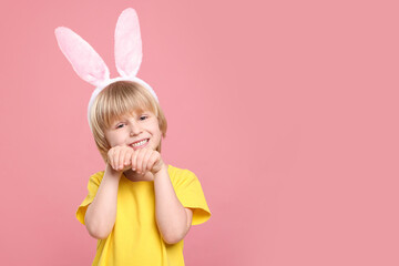 Happy boy wearing bunny ears headband on pink background, space for text. Easter celebration