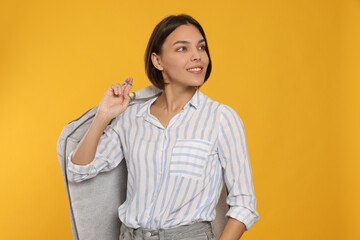 Woman holding garment cover with clothes on yellow background. Dry-cleaning service