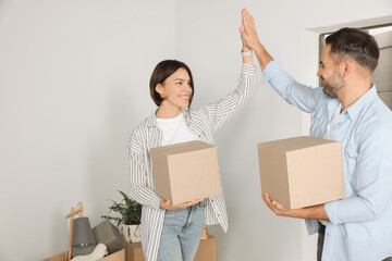 Happy couple with moving boxes giving high five in new apartment