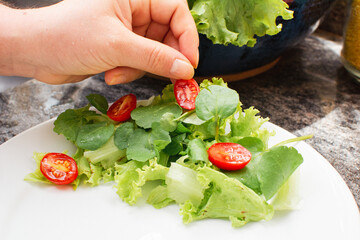Woman's hand serving cherry tomato and mixed leafy greens salad on a plate