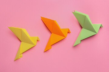 Beautiful colorful origami birds on pink background, flat lay