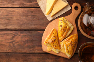 Fresh delicious puff pastry served with cheese and tea on wooden table, flat lay. Space for text
