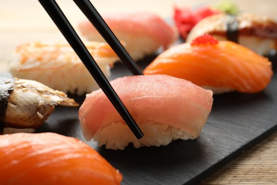 Taking delicious nigiri sushi with chopsticks on wooden table, closeup