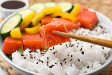 Chopsticks with salmon over delicious poke bowl , closeup