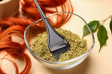 Bowl of henna powder, brush, green leaves and red strand on beige background, closeup. Natural hair...