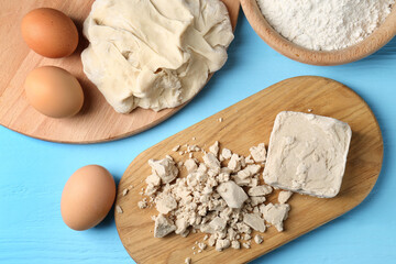 Pieces of compressed yeast, eggs, dough and flour on light blue wooden table, flat lay