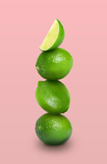 Stacked whole and cut limes on pink background