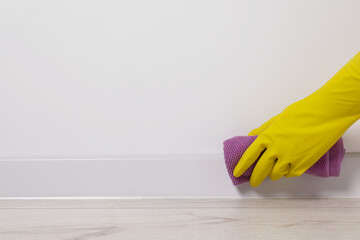 Woman in protective glove cleaning plinth with washcloth indoors, closeup. Space for text