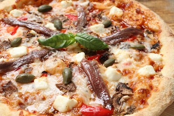 Tasty pizza with anchovies, basil and olives on wooden table, closeup