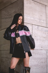 Urban chic: young brunette model wears leather jacket and long boots in big stone building with morning sunlight