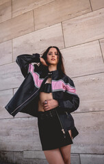 Urban chic: young brunette model wears leather jacket and long boots in big stone building with morning sunlight