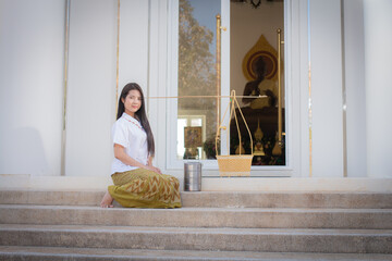 Beautiful thai woman in a white traditional thai dress is sitting and looking to the camera next to...