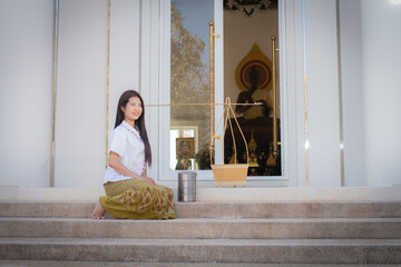 Beautiful thai woman in a white traditional thai dress is sitting and looking towards the copy...
