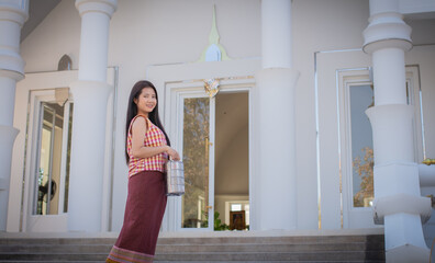 Beautiful thai woman in traditional thai dress standing and looking to to the camera while holding...